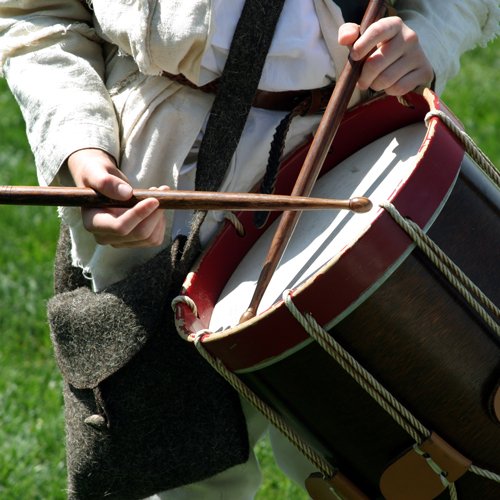 hands using drum sticks on drum with individual in Revolution War attire