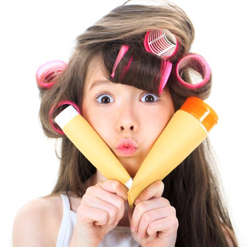 Young individual with hair rollers in hair and holding tubes of cosmetic cream