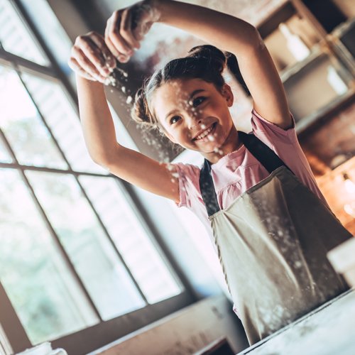 young child in apron sprinkling four on table