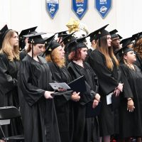 Graduates in cap and gown stand during commencement ceremony
