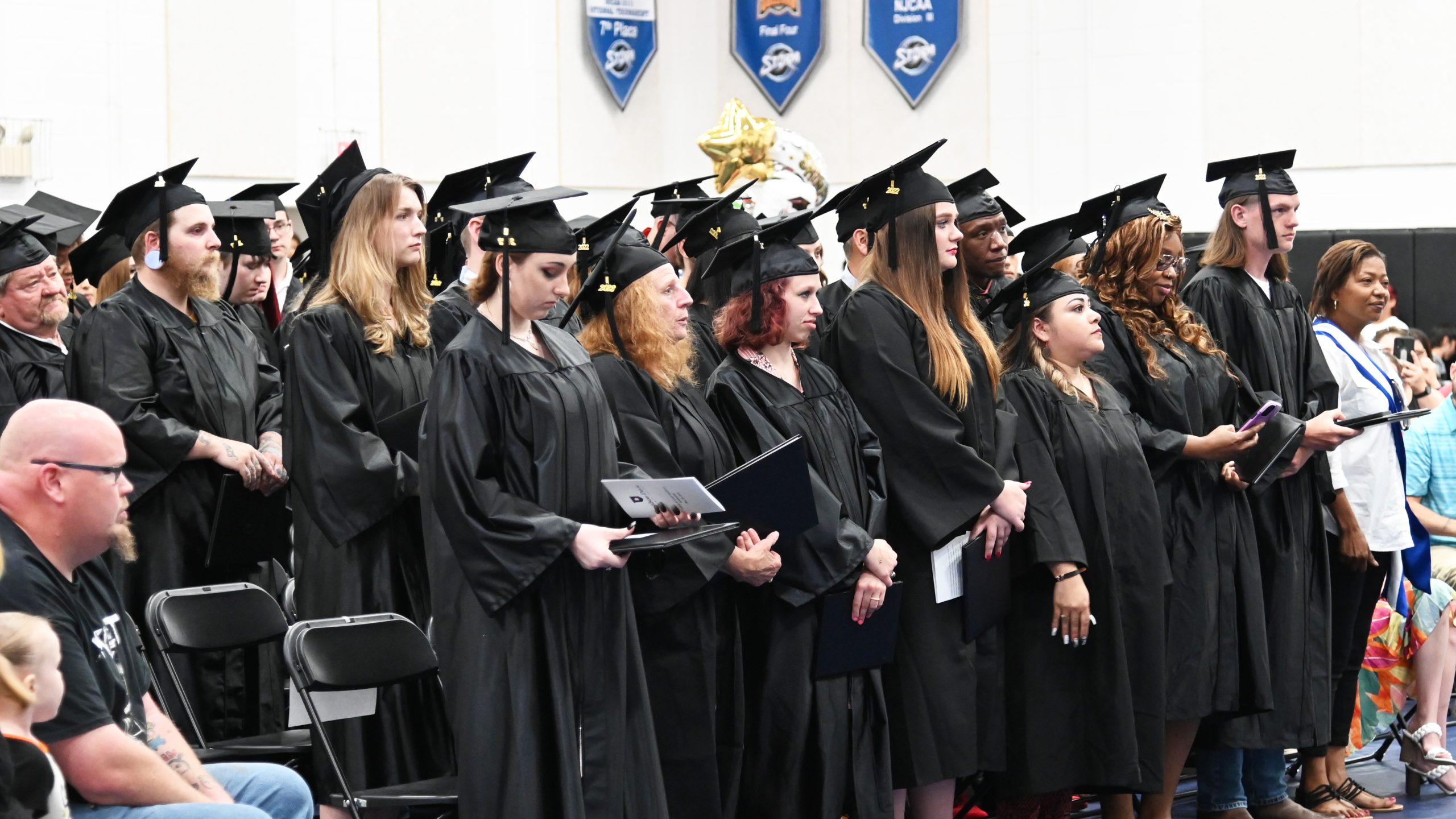 Graduates in cap and gown stand during commencement ceremony