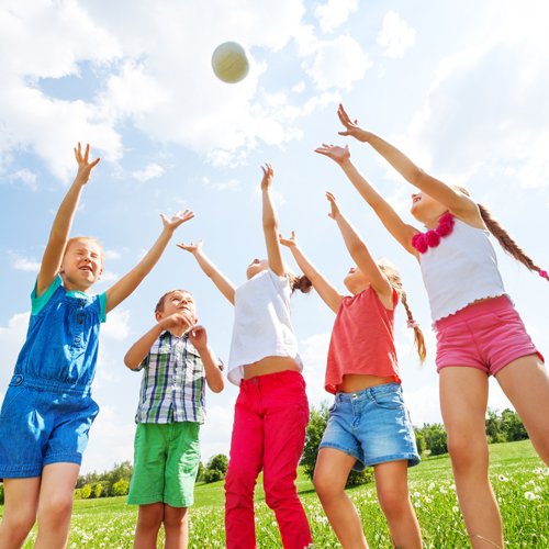 Brightly clothed children reaching for ball in air