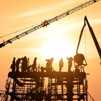 Workers on skyscraper being built with sun setting in background