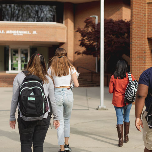 Group of students with backpacks with back to camera heading toward bricked building