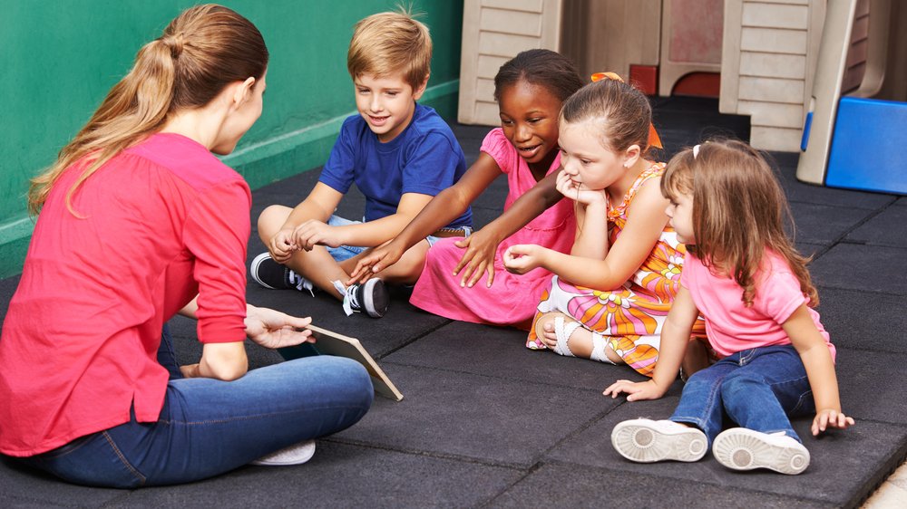 Young teacher sitting on floor with 4 young children