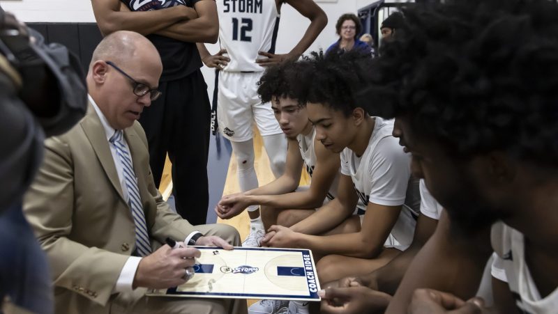 Storm Basketball Coach draws up play while team watches