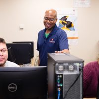 Information Technology Instructor helps two students at computers