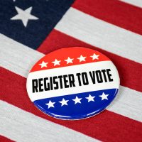Patriotic button that says "Register To Vote" laying on top of American flag.