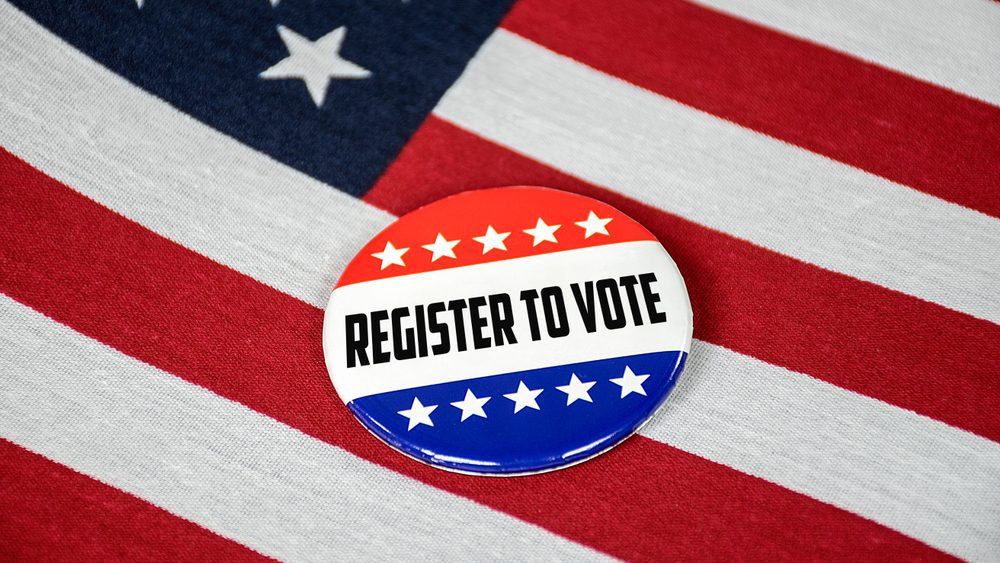 Patriotic button that says "Register To Vote" laying on top of American flag.
