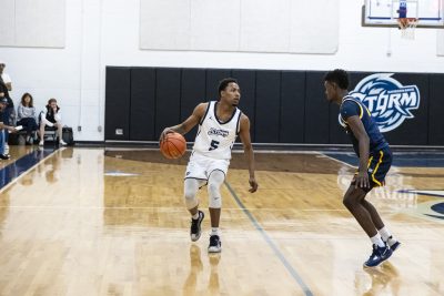Two basketball players on an indoor court during a game, with one dribbling the ball.