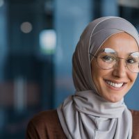 Woman wearing hijab and glasses smiling at camera