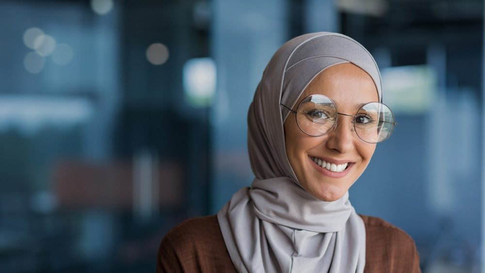 Woman wearing hijab and glasses smiling at camera