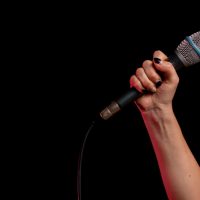 Woman's hand holding wired microphone in front of black background