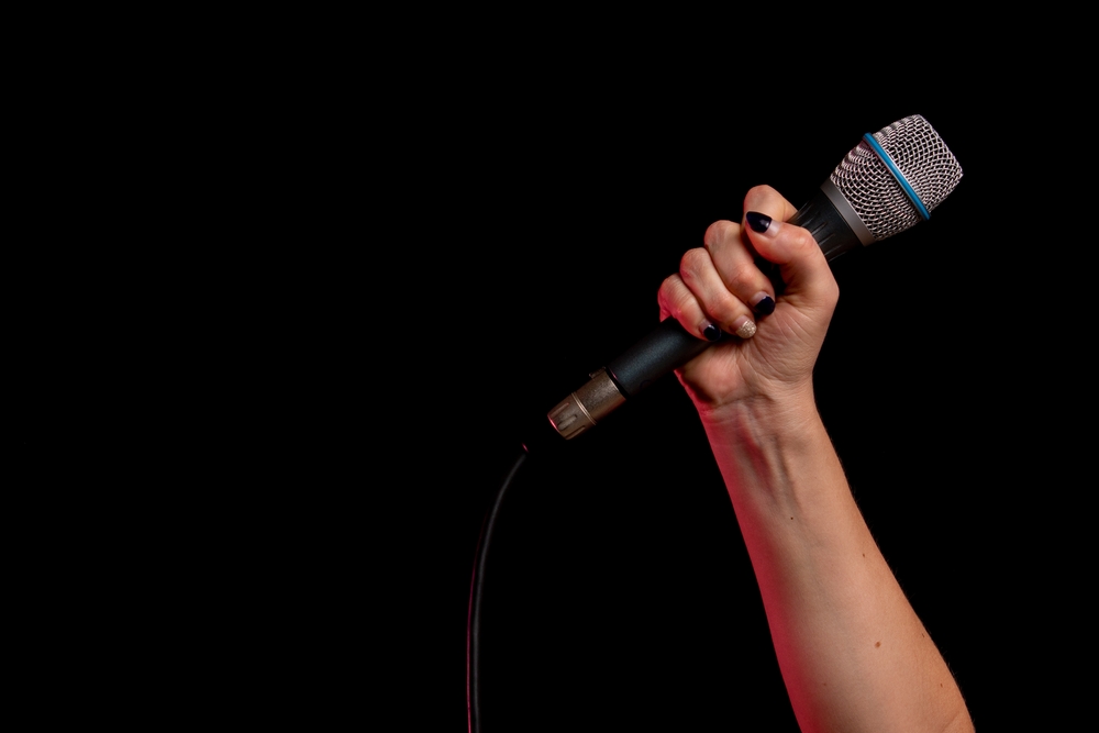 Woman's hand holding wired microphone in front of black background