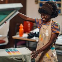 young girl smiling while screen printing a shirt