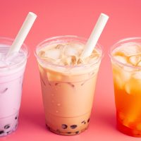 Three cups of bubble tea with straws on a pink background.