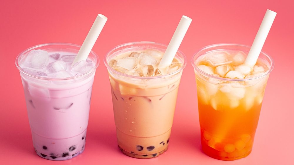 Three cups of bubble tea with straws on a pink background.
