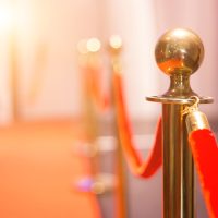 Close-up of a shiny metal stanchion with a red velvet rope on a red carpet.