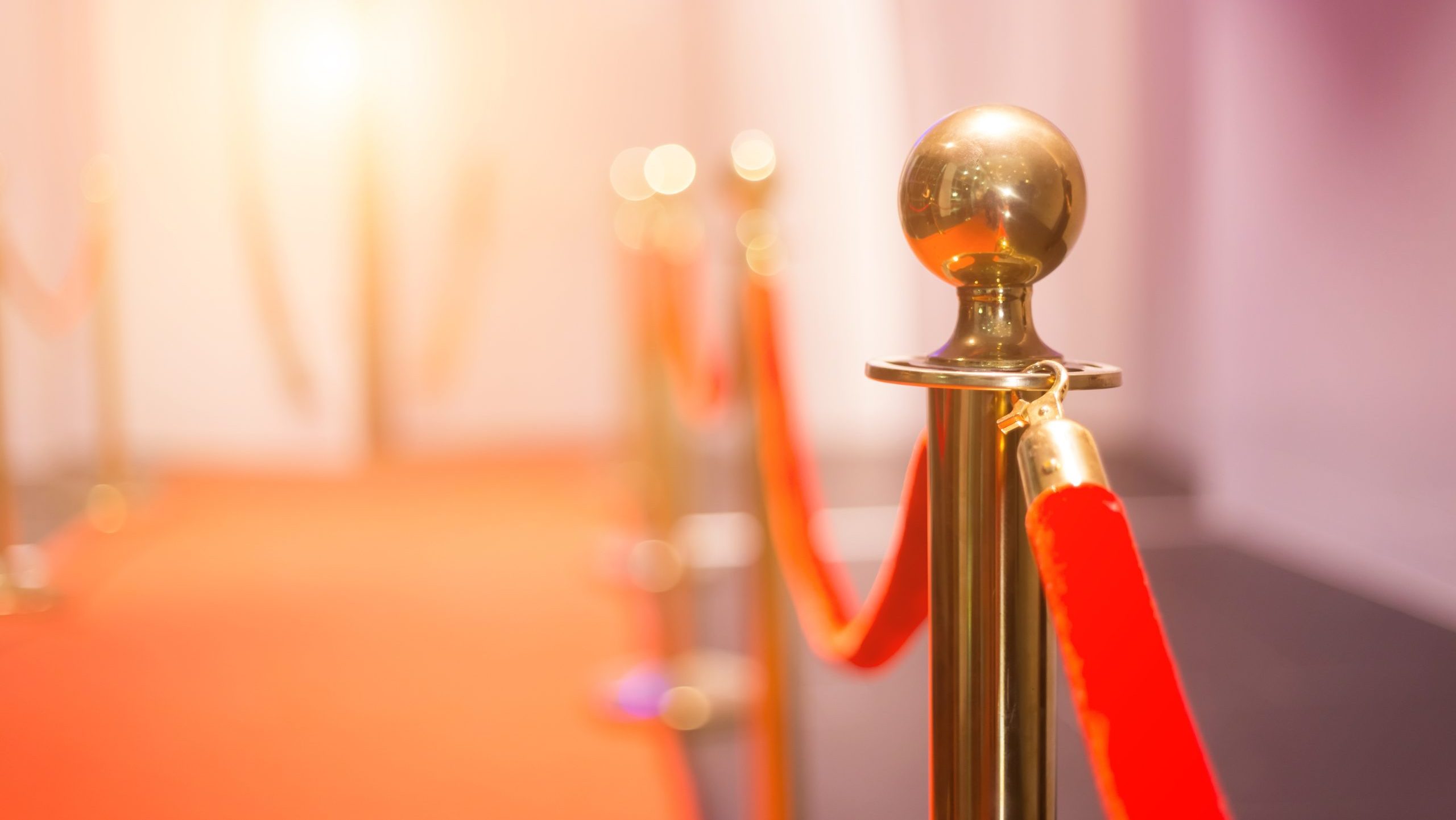 Close-up of a shiny metal stanchion with a red velvet rope on a red carpet.