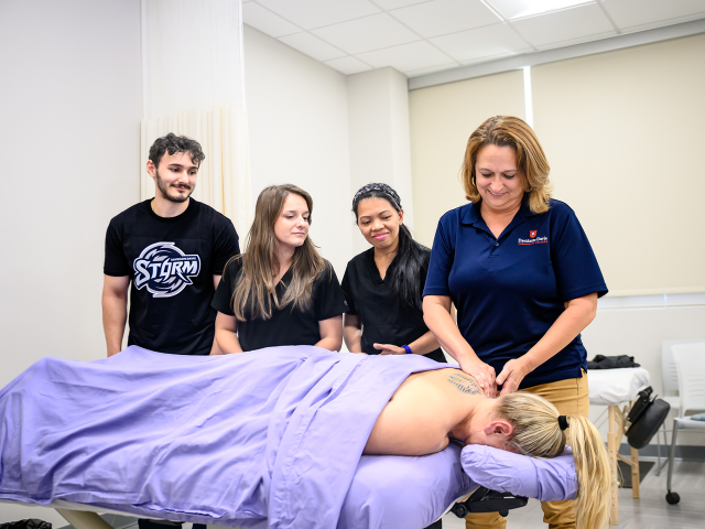 A group of people around a massage table with one person giving a massage.