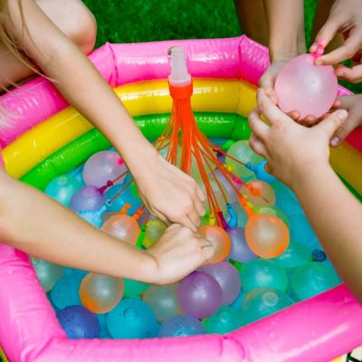 Water,Balloon,Games,For,Kids.,Close,Up,Of,Girls,Filling Children playing with colorful water balloons in a small inflatable pool.