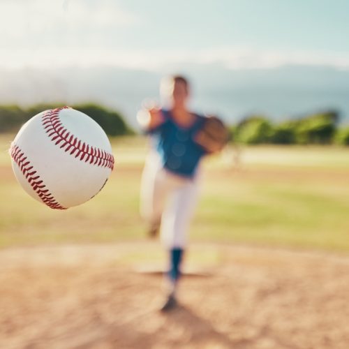 Baseball,,Sport,And,Ball,With,A,Sports,Athlete,Or,Pitcher Baseball in the foreground with a blurred out baseball player in the background.
